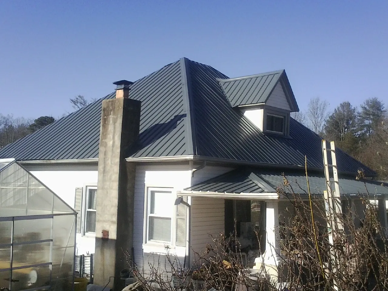 Dark blue standing seam metal roof on a white farmhouse with dormer — Slate & Tile Roof Repair by Roofing Brothers in Bishopville