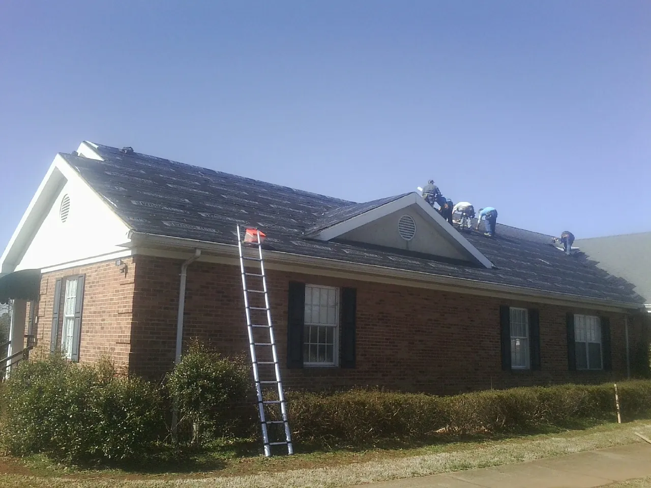 Crew tearing shingles off a brick ranch roof with a ladder set — Emergency Roof Repair work by our crew in Bishopville
