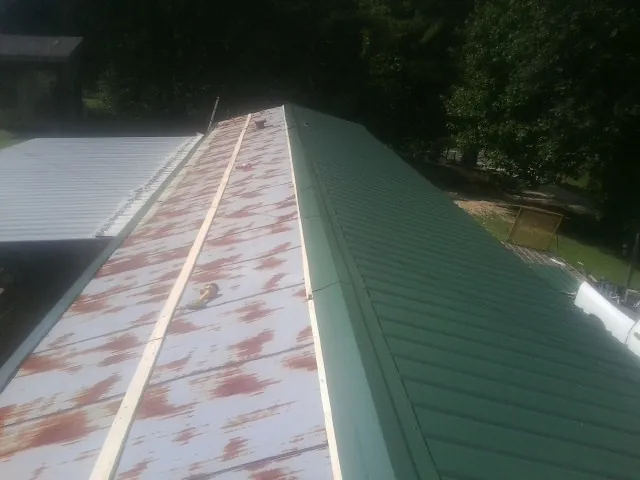 Old rusted panels beside newly installed green metal roofing — Wind Damage Roof Repair by Roofing Brothers in Bishopville