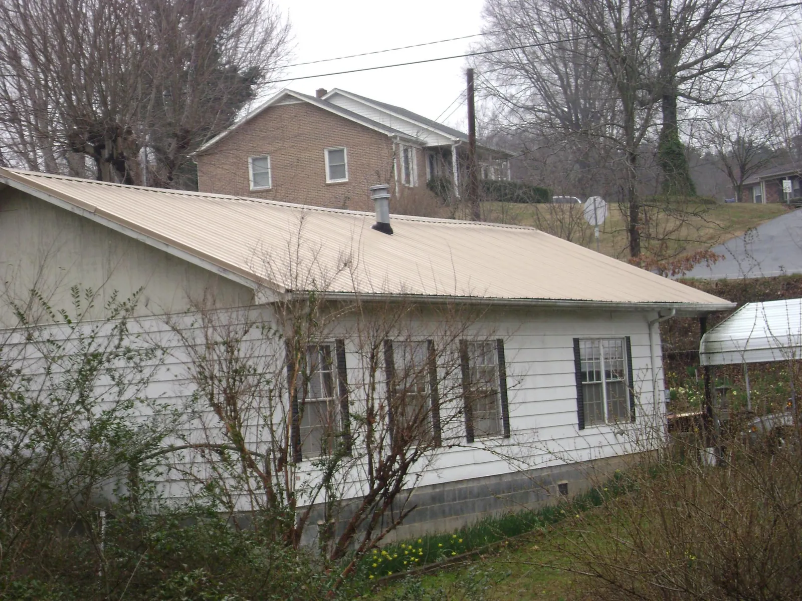 Tan metal roof on a white sided house set into a hillside — Commercial Roofing by Roofing Brothers in Bishopville
